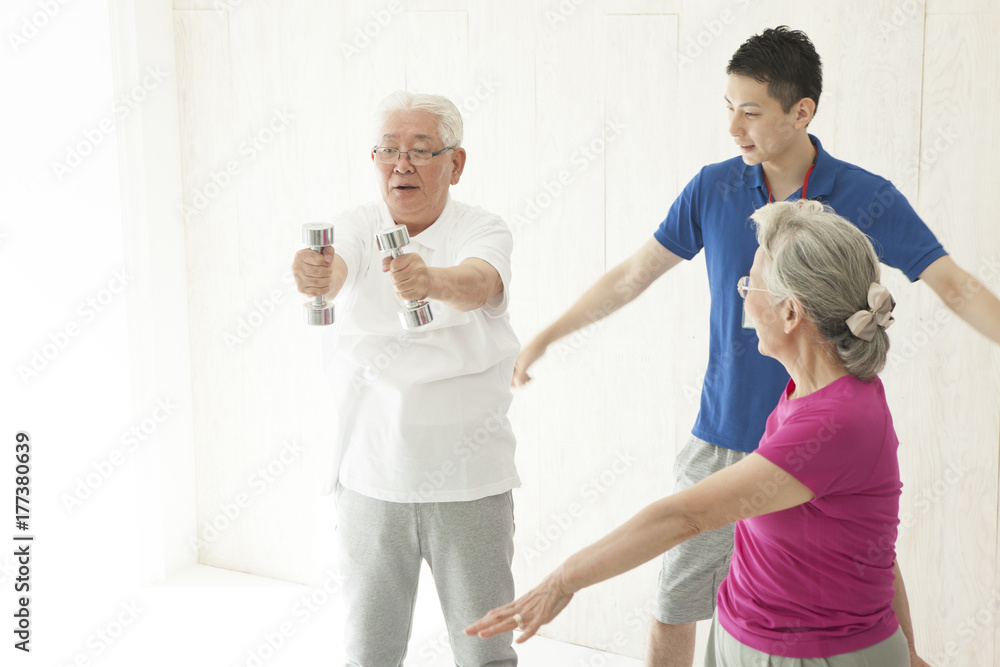 An elderly couple is doing dumbbell training with a trainer