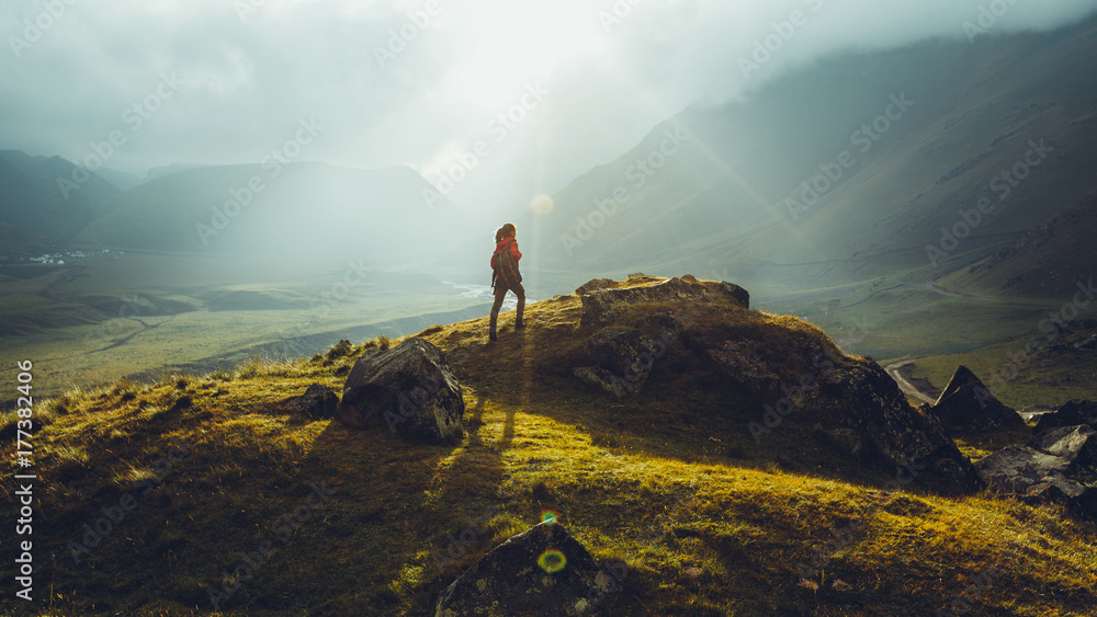 Hiker Young Woman With Backpack Rises To The Mountain Top Against Backdrop Of Sunset. Discovery Travel Destination Concept - obrazy, fototapety, plakaty 