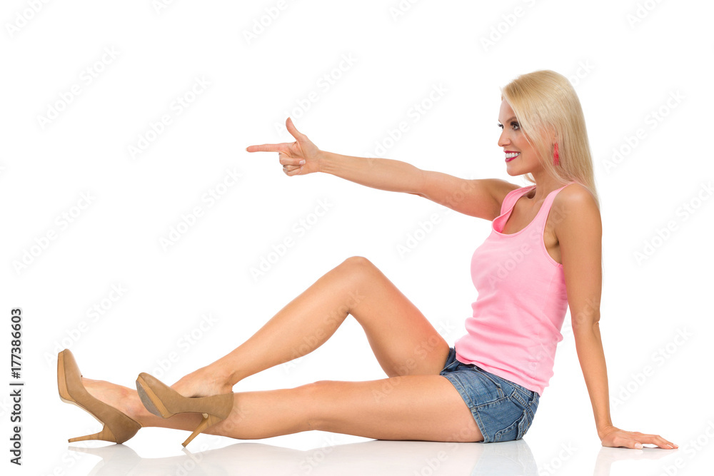 Beautiful Blond Smiling Woman Is Sitting On Floor And Pointing. Side View. Beautiful Blond Smiling Woman Is Sitting On Floor And Pointing. Side View.