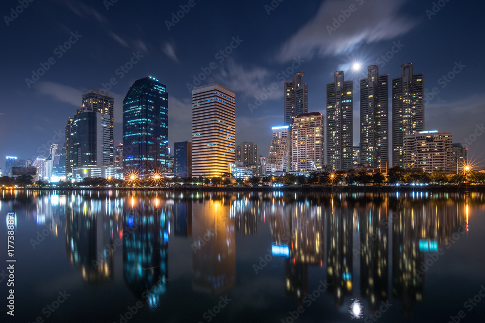 Fototapeta premium Benjakiti Park in Bangkok, Thailand. In the night with calm water reflecting buildings, moving cloud on the sky.