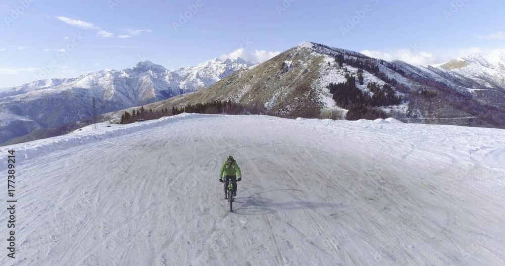 backward aerial over biker man cycling on snowy path during winter with mtb e-bike. Cyclist on bike on snow outdoors in winter. 4k drone flight video backward aerial over biker man cycling on snowy path during winter with mtb e-bike. Cyclist on bike on snow outdoors in winter. 4k drone flight video