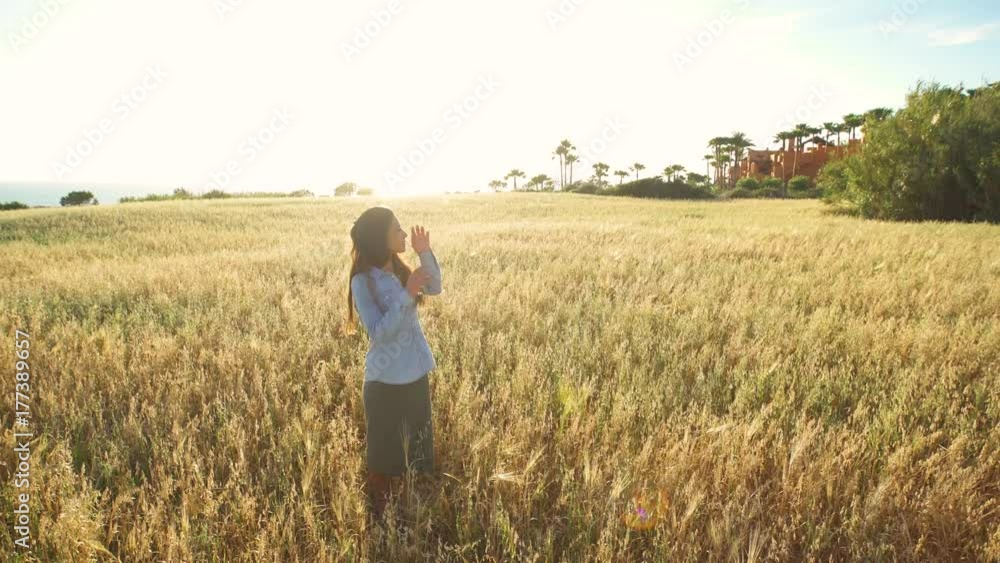 Beautiful girl walking and upping her arms in a wheat field with the sun behind Beautiful girl walking and upping her arms in a wheat field with the sun behind