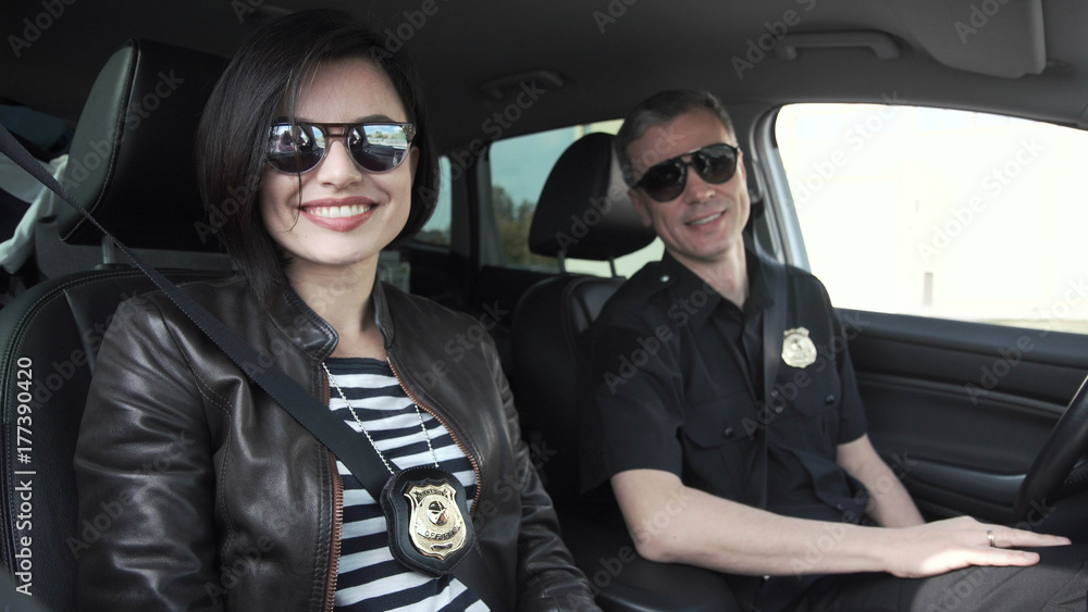 Female and male smiling police officers with badges sitting in car Female and male smiling police officers with badges sitting in car