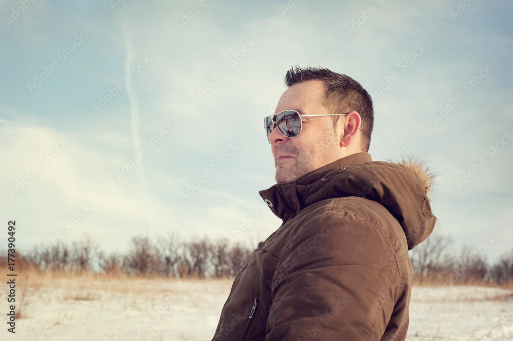 Man viewing the winter scenery wearing sunglasses with blue sky and trees in the background Man viewing the winter scenery wearing sunglasses with blue sky and trees in the background