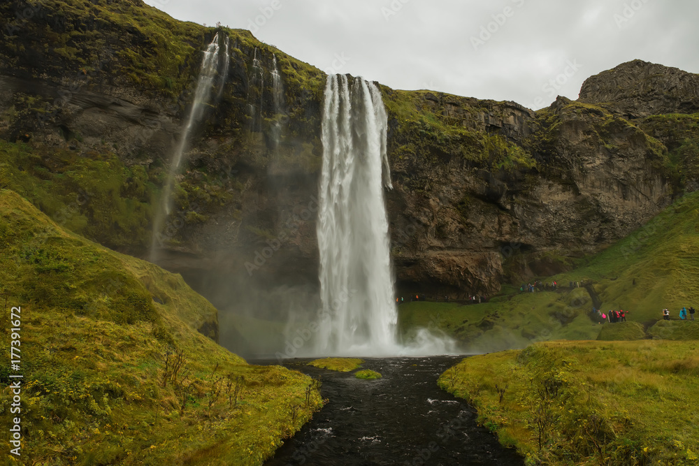 A number of steep cliffs on the right and a huge waterfall. Gloomy, severe weather, gloomy sky. Everything is shrouded in smoke from the waterfall. Nature and sights of Iceland.
A number of steep cliffs on the right and a huge waterfall. Gloomy, severe weather, gloomy sky. Everything is shrouded in smoke from the waterfall. Nature and sights of Iceland.