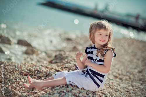 Stylish dressed blond child girl enjoy posing summer vacation on public city beach wearing casual bright clothes happy smiling on camera alone