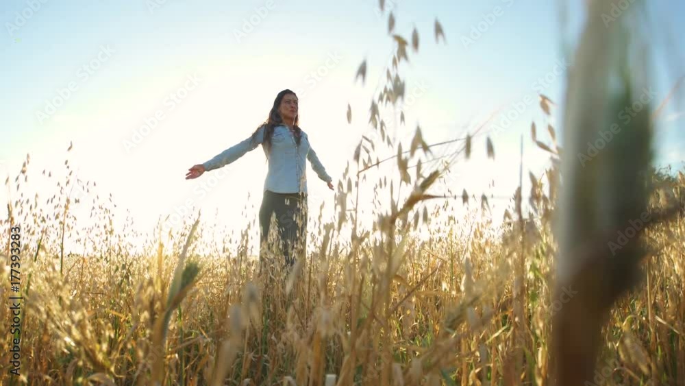 Beautiful girl walking and upping her arms in a wheat field with the sun behind Beautiful girl walking and upping her arms in a wheat field with the sun behind