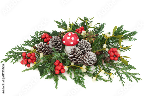 Christmas fantasy table decoration with fly agaric mushroom, holly, ivy, mistletoe, cedar and juniper leaf sprigs and pine cones on white background.