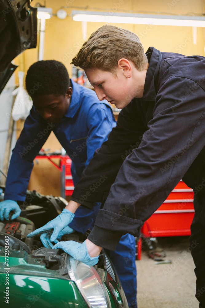 Two young apprentice mechanics repairing a vehicle in a garage. Two young apprentice mechanics repairing a vehicle in a garage.