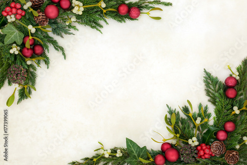 Christmas decorative background border on parchment paper with red bauble decorations, holly, mistletoe, ivy, fir and pine cones. 