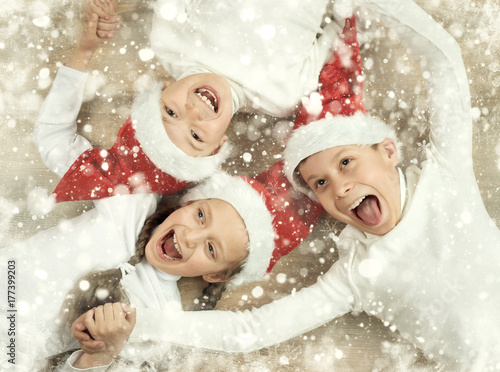 happy child lying together on wooden background, dressed in christmas Santa hat and having fun, winter holiday concept, snow decoration, yellow toned