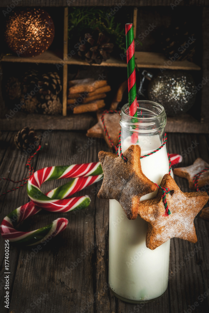 Obraz premium Christmas sweet and treats, Bottles with milk for Santa with gingerbread star cookies with decoration rope and christmas decorations, old wooden background, copy space