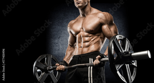 Young sexy bodybuilder with perfect body doing exercise with barbell on black background.