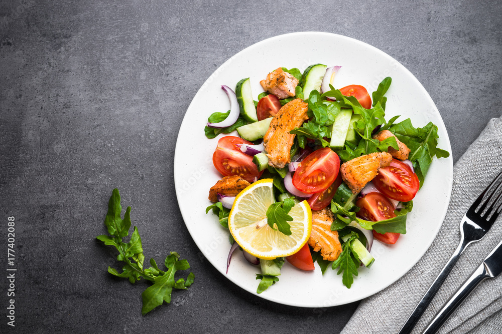 Fresh salad with salmon and vegetables on black background.