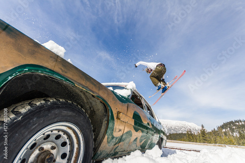 Ski freestyle - Skier jumping over old abandoned racing car from a low angle point of view photo