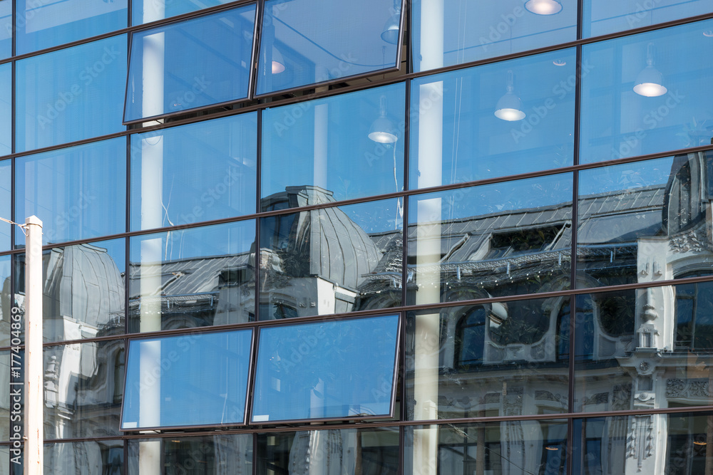 Reflection of an old building in a modern glass facade, contrast of urban architecture, blue sky on a sunny day