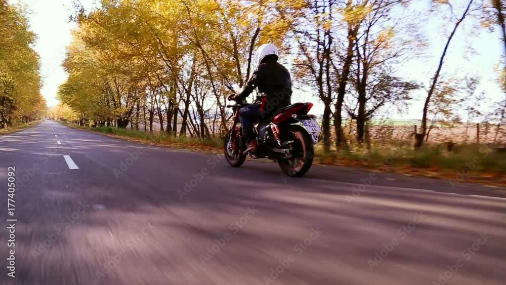 Man in white helmet riding motorcycle on country road at autumn sunset. Man in white helmet riding motorcycle on country road at autumn sunset.