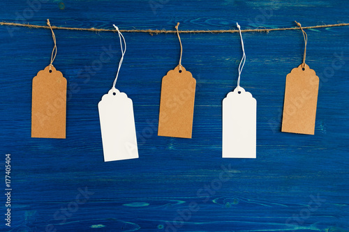 Five brown and white blank paper price tags or labels set hanging on a rope on the blue wooden background.