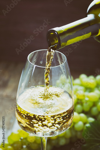 Pouring white wine into the glass against wooden background