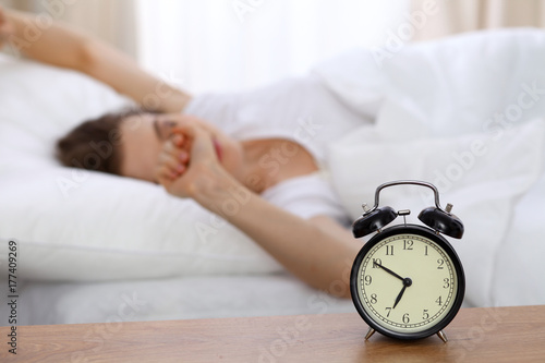 Beautiful sleeping woman resting in bed and trying to wake up with alarm clock