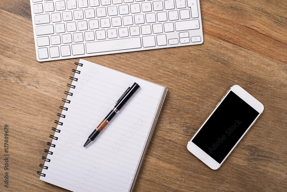 Keyboard and smartphone next to a notebook and pen on wooden table. Worplace. Keyboard and smartphone next to a notebook and pen on wooden table. Worplace.