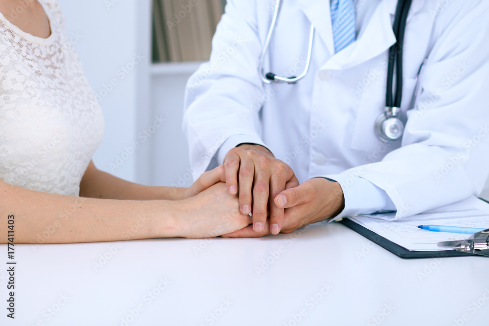 Doctor reassuring his female patient by touching her hands while talking. Symbol of support and trust in medicine Doctor reassuring his female patient by touching her hands while talking. Symbol of support and trust in medicine