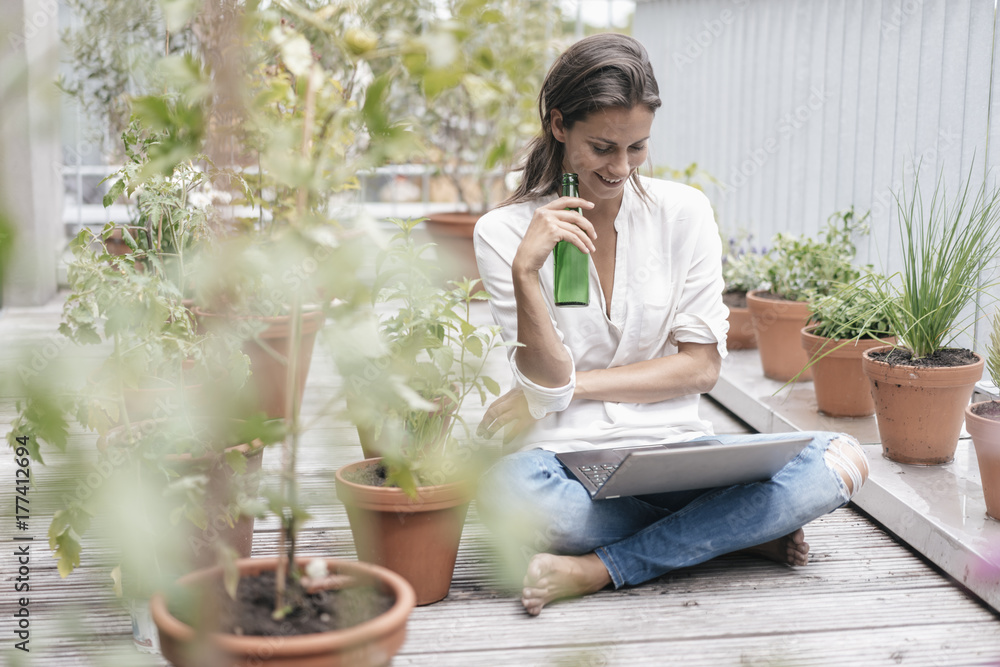 Smiling woman with laptop and bottle sitting on balcony Smiling woman with laptop and bottle sitting on balcony