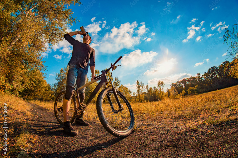 Obraz premium young man drinks a protein shake from a shaker while taking a bike