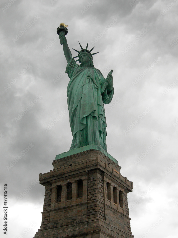 Fototapeta premium Statue of liberty seen from the front with a grey and cloudy sky as background in Manhattan, New York City..
