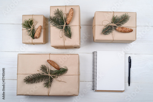 Top view of blank notebook on white wooden background with xmas decorations, copy space. Christmas background with notebook for wish list or to do list and gift boxes with fir tree branches. Flat lay
