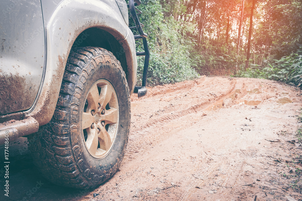 Car wheel on a dirt road. Off-road tire covered with mud, dirt terrain. Outdoor, adventures and travel. Car tire close-up in a countryside landscape with a muddy road. Four wheel truck in mud.