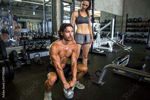 Billede på lærred Physical trainer at local coed gym showing female how to lift a kettle bell squa