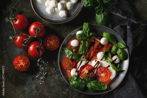Italian caprese salad with sliced tomatoes, mozzarella cheese, basil, olive oil. Served in vintage metal plate with ingredients above over dark metal background. Top view with space. Rustic style