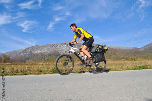 Traveler rides a bicycle on road under a mountain. Cyclist on the road on sunny autumn day