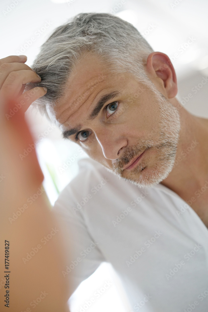 40-year-old man checking hair in front of mirror Stock Photo | Adobe Stock