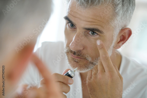 Portrait of middle-aged man applying eye concealer
