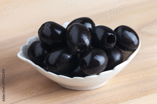 White bowl with black olives on wooden table