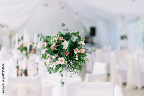 Beautiful wedding floral decoration on a table in a restaurant. White tablecloths, bright room, candles, close-up shooting. The event, happiness, honeymooners. Soft bokeh white background