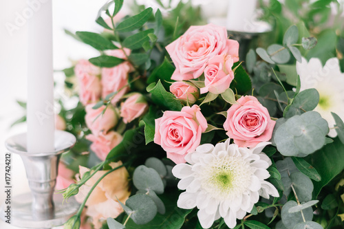 Beautiful wedding floral decoration on a table in a restaurant. White tablecloths  bright room  candles  close-up shooting. The event  happiness  honeymooners. Soft bokeh white background