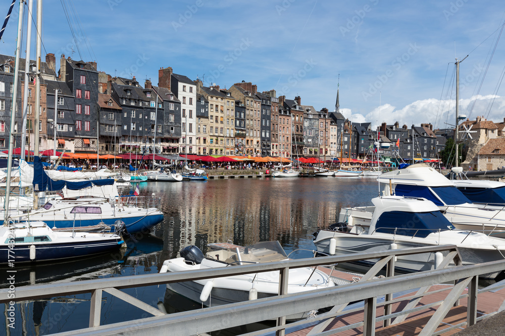 Saling boats in old medieval harbor of Honfleur, France. Tourists are relaxing at terraces along the harbor.
