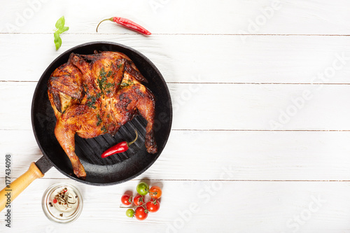 Grilled chicken on grill pan with tomatoes oil basil and chili on white wooden table top view