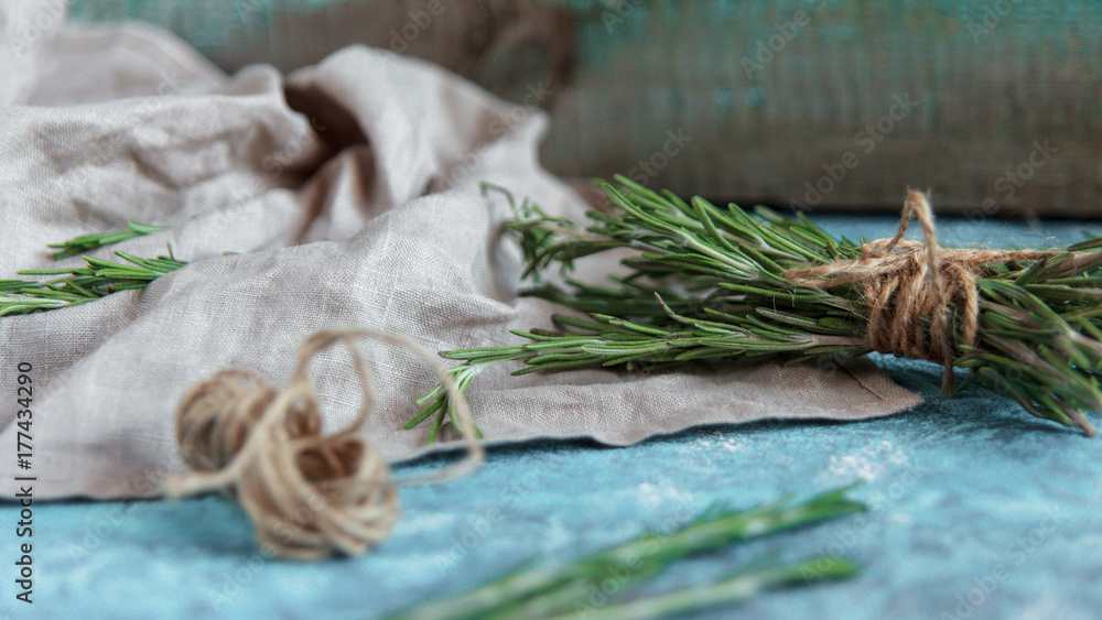 A bunch of fresh rosemary on linen cloth, Rustic greenery on blue wooden background. A bunch of fresh rosemary on linen cloth, Rustic greenery on blue wooden background.