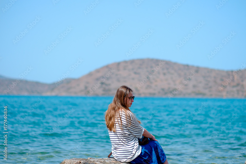 young beautiful girl sitting on a pier looking at the sea and mountains