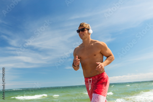 happy man with headphones running along beach