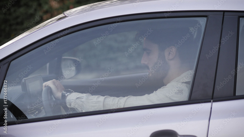 Serious young man or teenager driving car and looking at camera Serious young man or teenager driving car and looking at camera