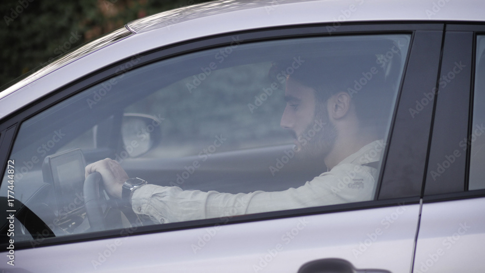 Serious young man or teenager driving car and looking at camera