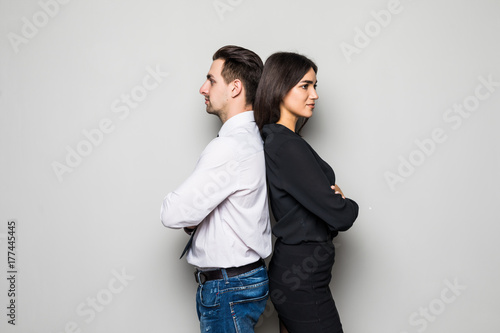 Attractive young couple standing back to back both staring thoughtfully into the distance with quiet smiles, on grey