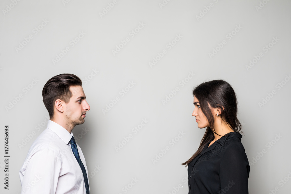 Concept of confrontation in business. Close up photo of two young serious confident people standing face-to-face to each other on gray Concept of confrontation in business. Close up photo of two young serious confident people standing face-to-face to each other on gray