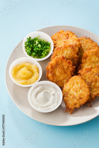 Potato pancakes, latkes or boxty and sauces from sour cream, yogurt, apple sauce and finely chopped green onion isolated on a blue background