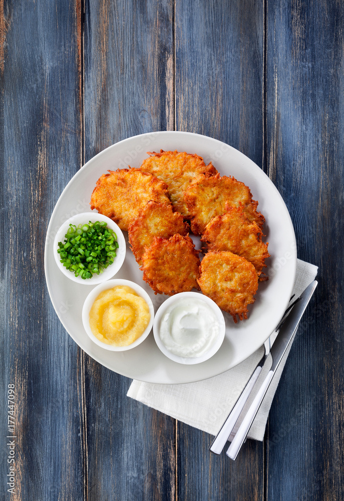 Potato pancakes, latkes or boxty and sauces from sour cream, yogurt, apple sauce and finely chopped green onion on a wooden table of boards Potato pancakes, latkes or boxty and sauces from sour cream, yogurt, apple sauce and finely chopped green onion on a wooden table of boards